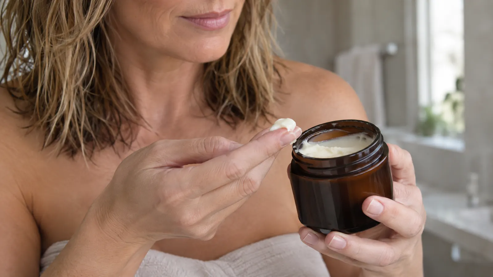 Hand scooping a small amount of hair mask from its container before applying it to damp hair